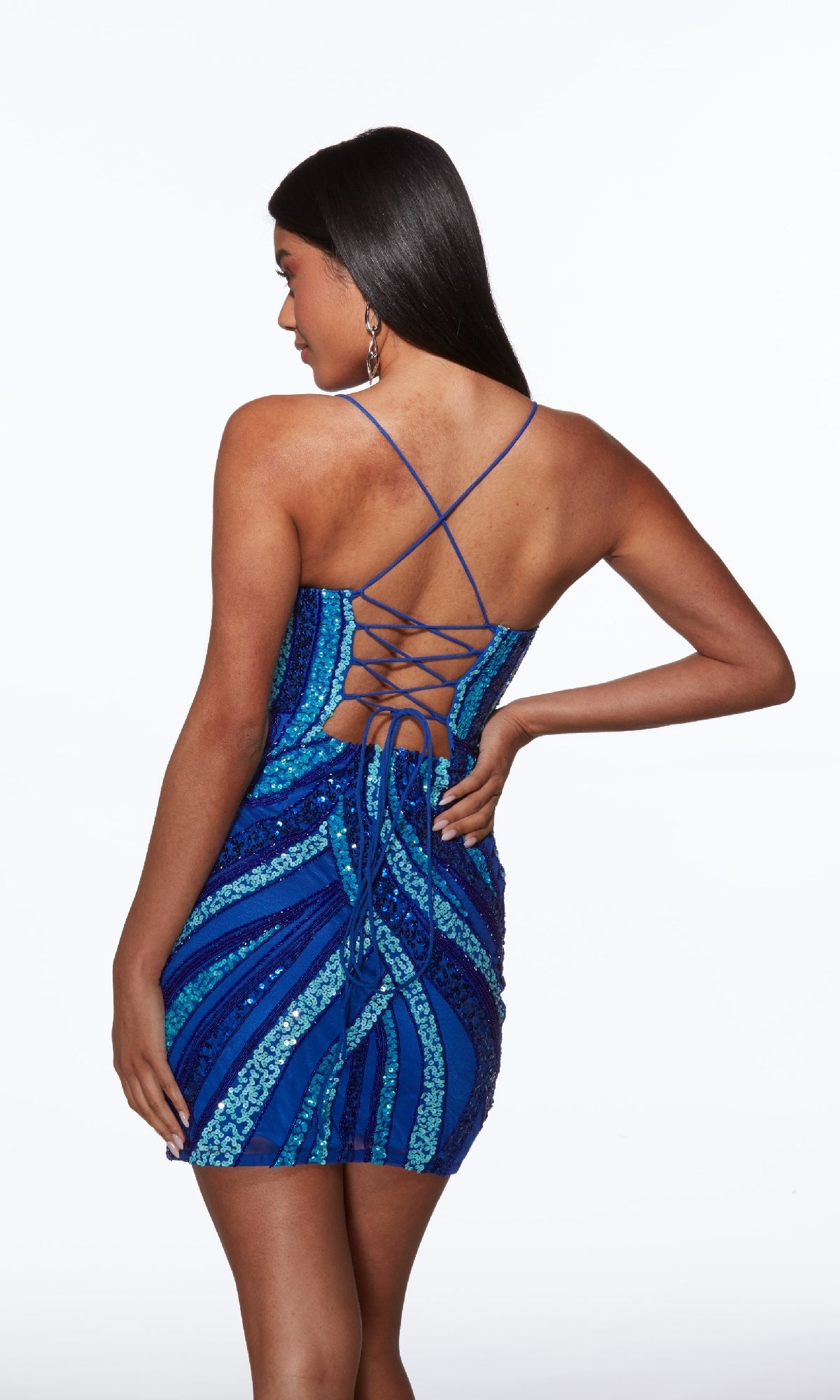 Woman models the Short Homecoming Dress: Alyce 40013, featuring blue sequins and a crisscross lace-up back, standing confidently against a white background—an ideal standout choice for homecoming.